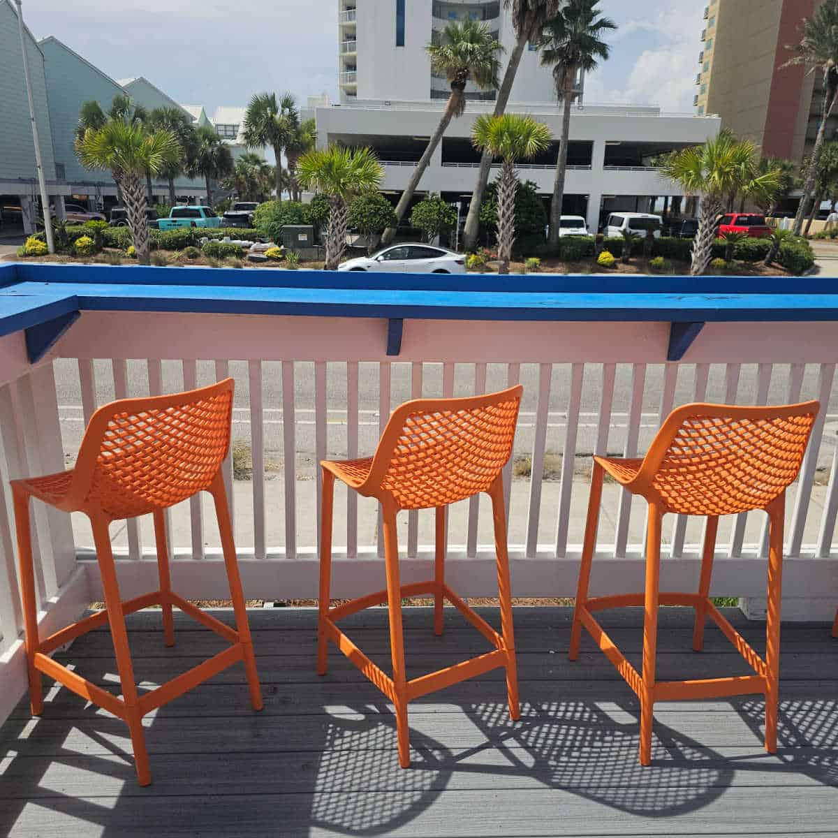 orange tall chairs next to a railing looking out over the road with a condo building behind it