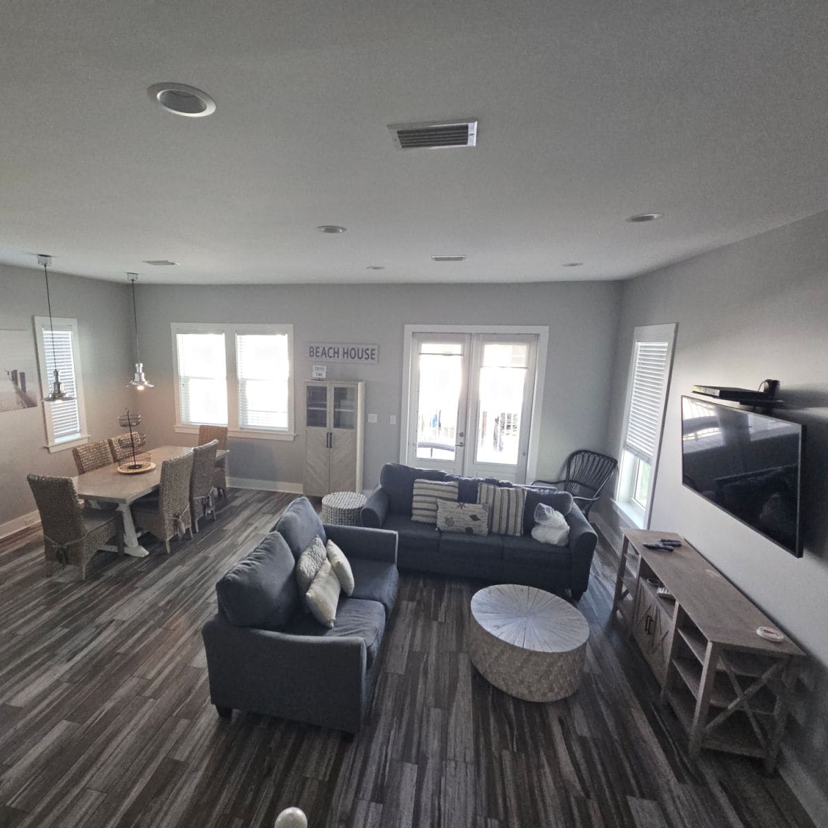 looking down into a living room and dining room with blue couches, circle table, and tv mounted on the wall, rattan chairs around a dining room table in the back corner