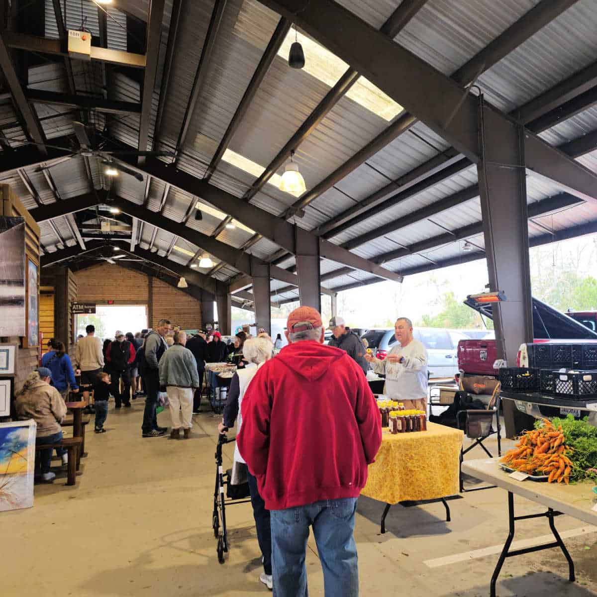 people walking through the farmers market with tables of vegetables and honey along the side