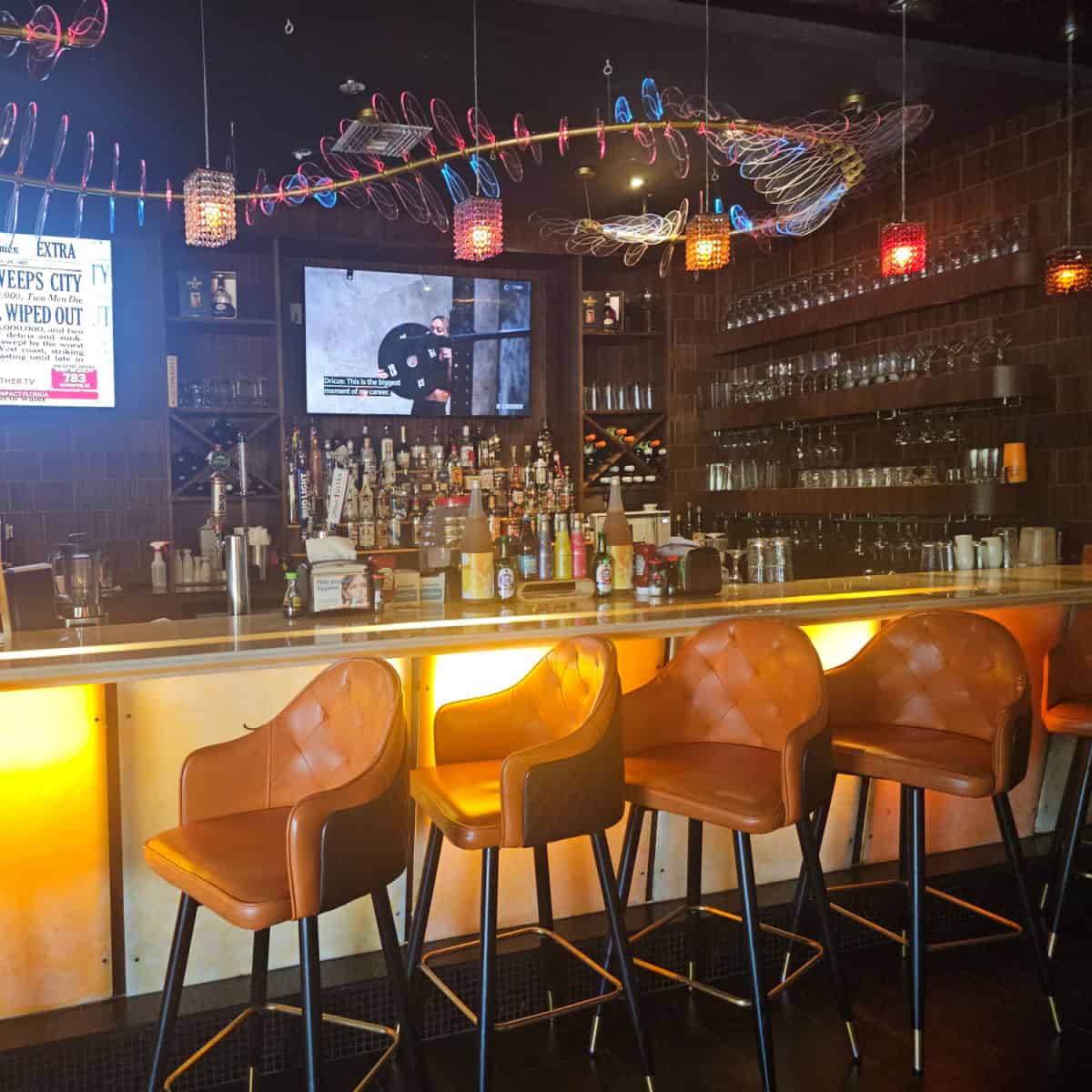 indoor bar with tall chairs, lights over the bar with glasses along the wall, bottles on the back bar