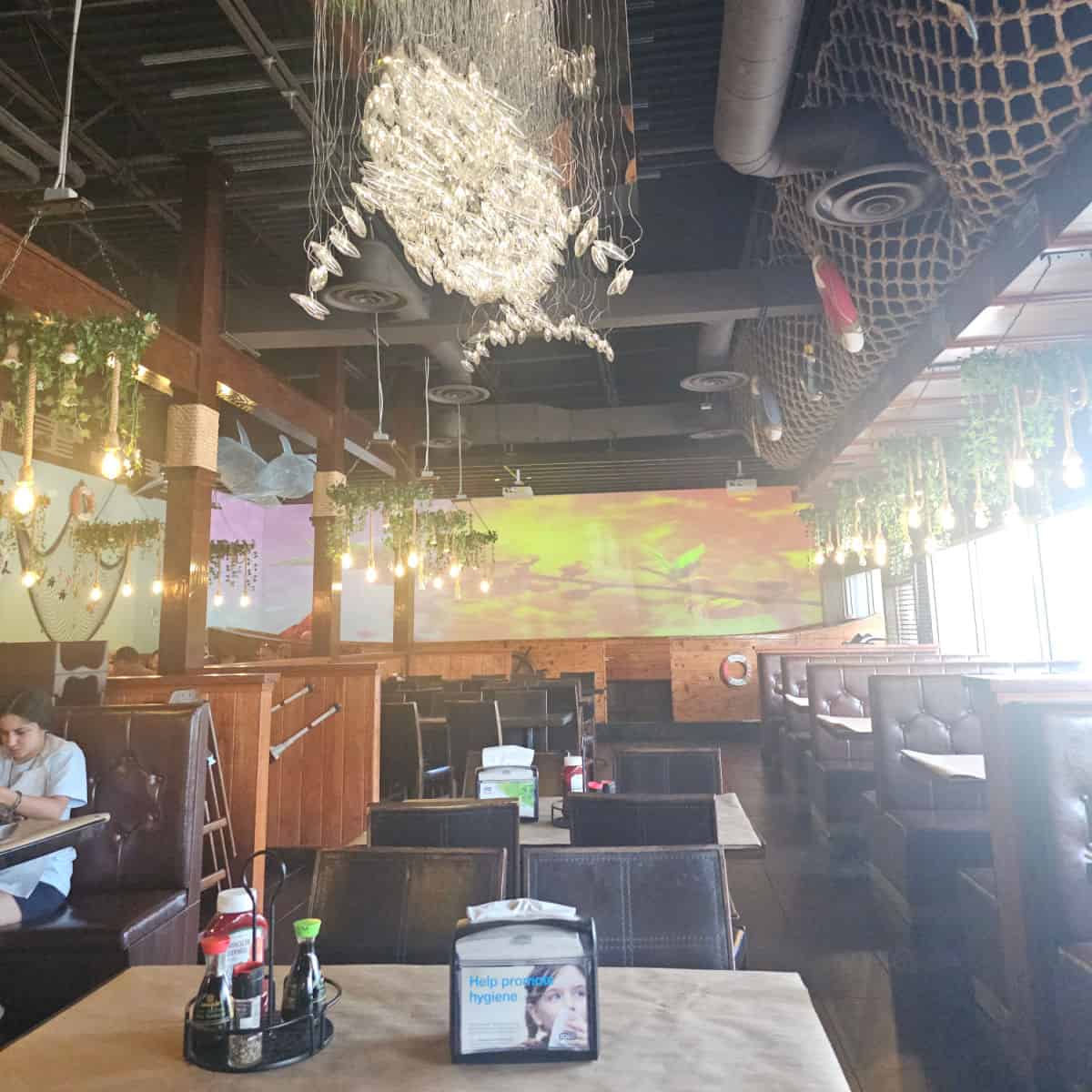 indoor seating with booths along two sides and row of tables down the middle, whale shaped light hanging from the ceiling, large screen on the back wall