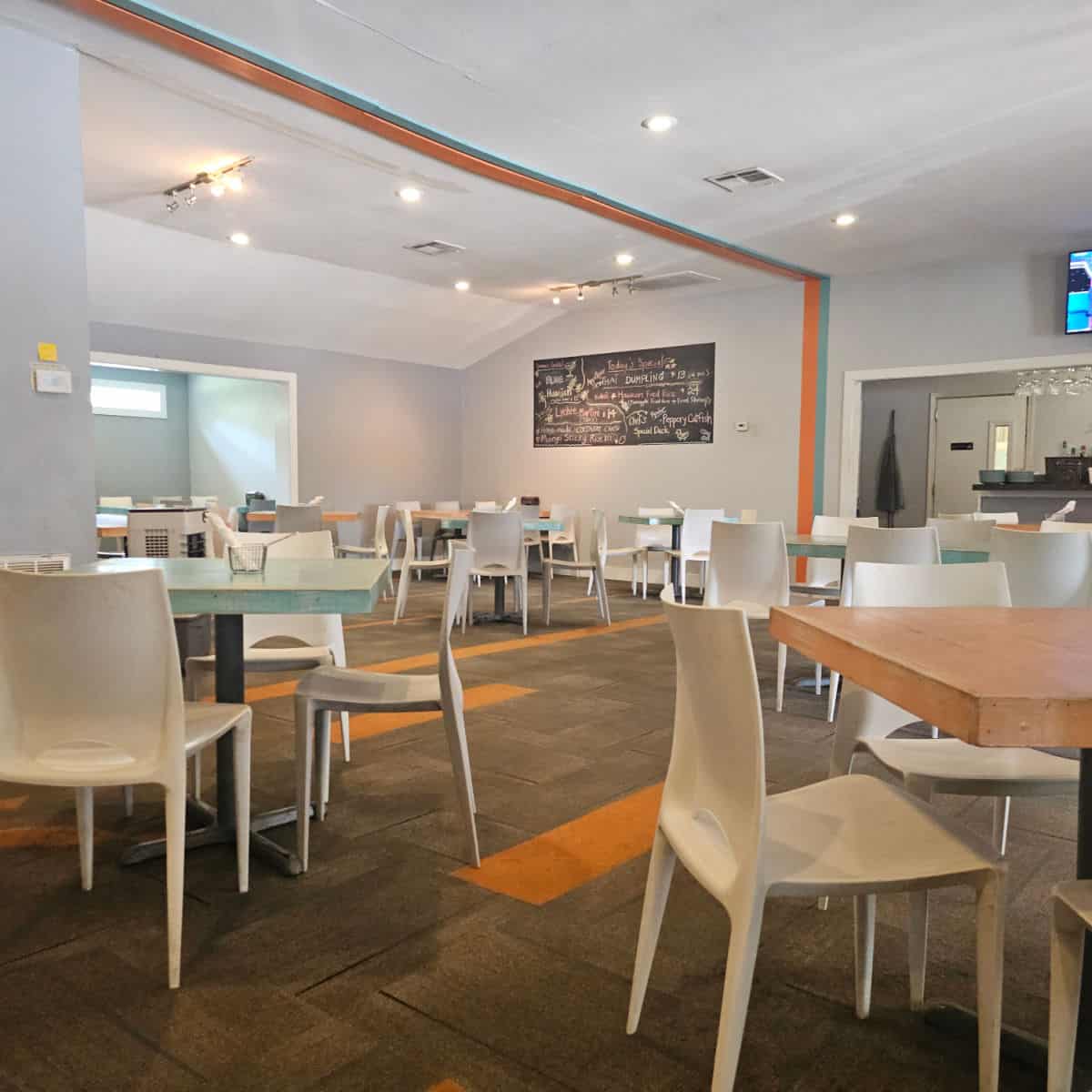 Niki's Thai indoor seating with tables and white plastic chairs spread around the room, chalkboard on the wall with menu specials