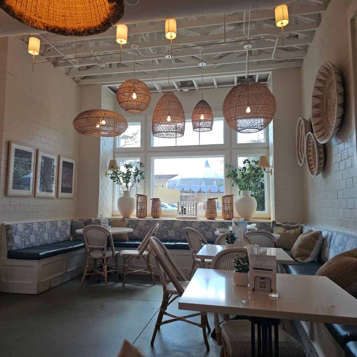 Press & Co interior with large basket weave lamps hanging from the ceiling, baskets on the wall, wrap around blue and white bench with white tables and extra chairs