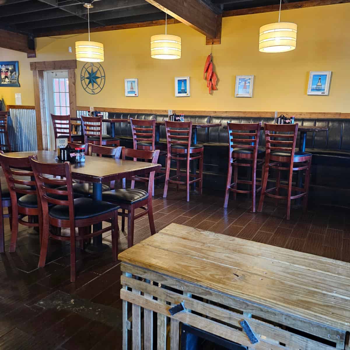 indoor seating with bench seating along the wall with tall tables and bar stools, low table in the middle with regular chairs, yellow walls with art on them