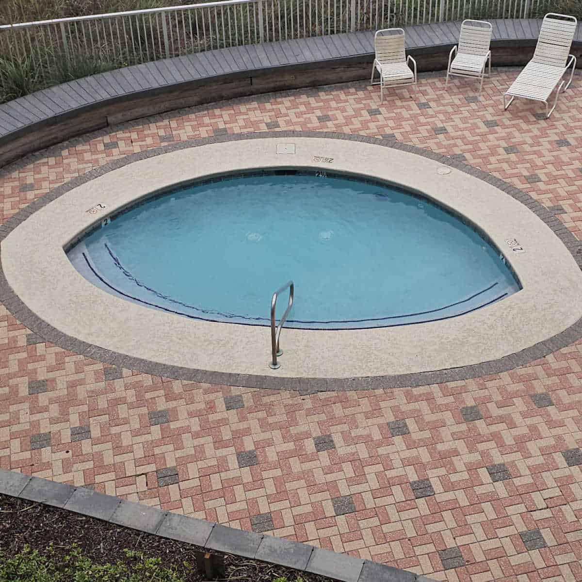 small pool shaped like an eye, pool lounge chairs on the pool deck by the fence