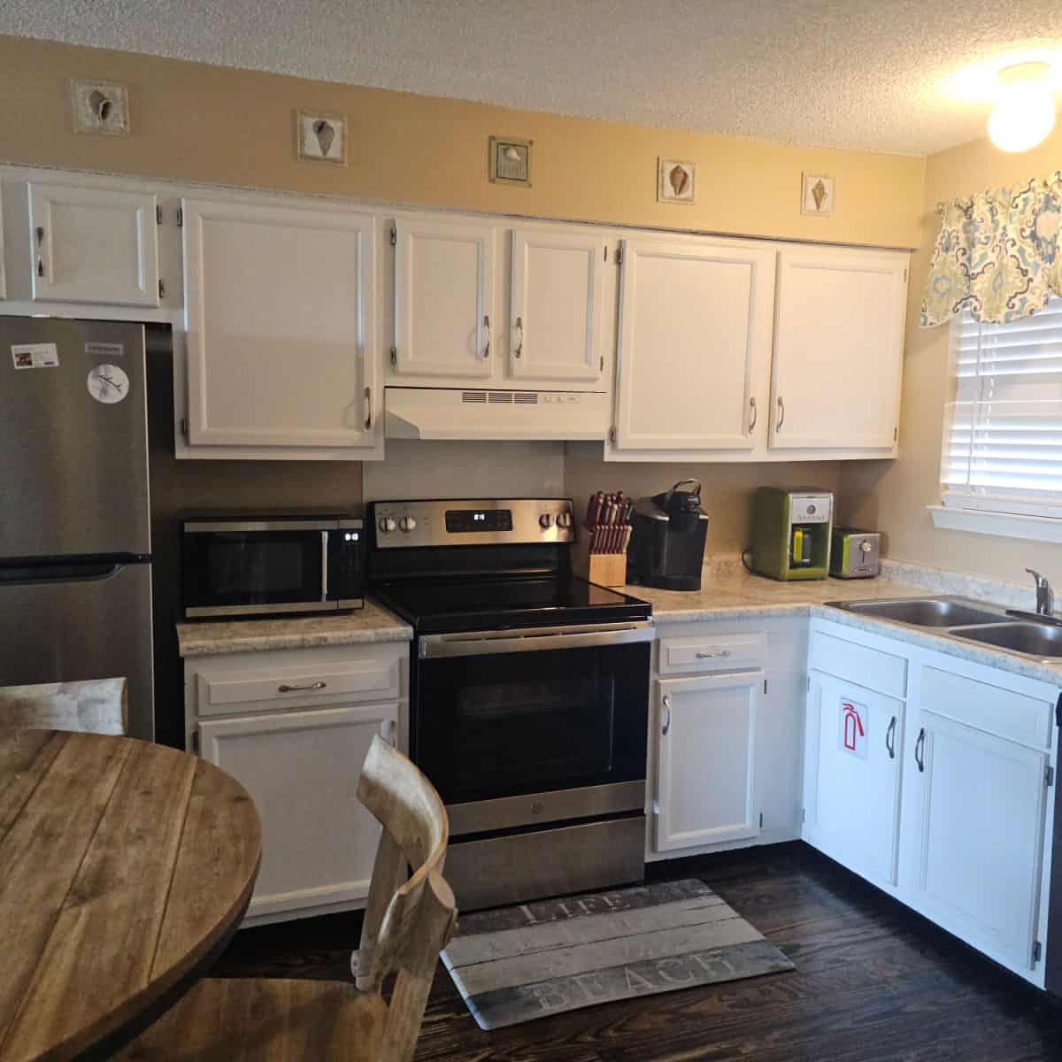 Kitchen area with white cabinets, stainless steel appliances and yellow walls portion of circle wooden table in the lower left corner