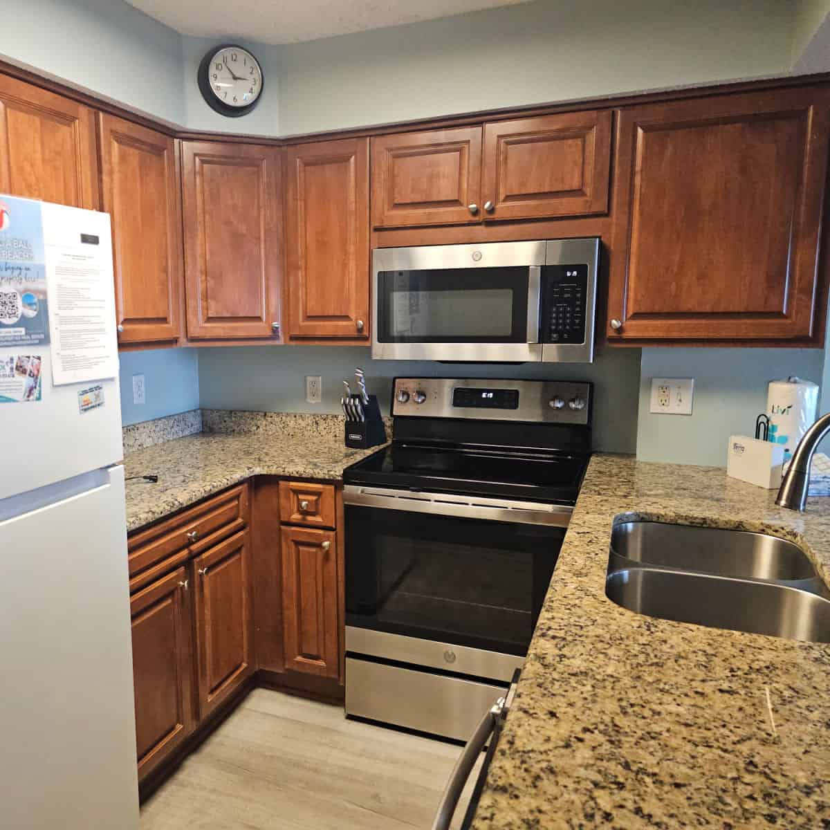 kitchen with brown cabinets, granite countertops, stainless steel oven and microwave, white refrigerator