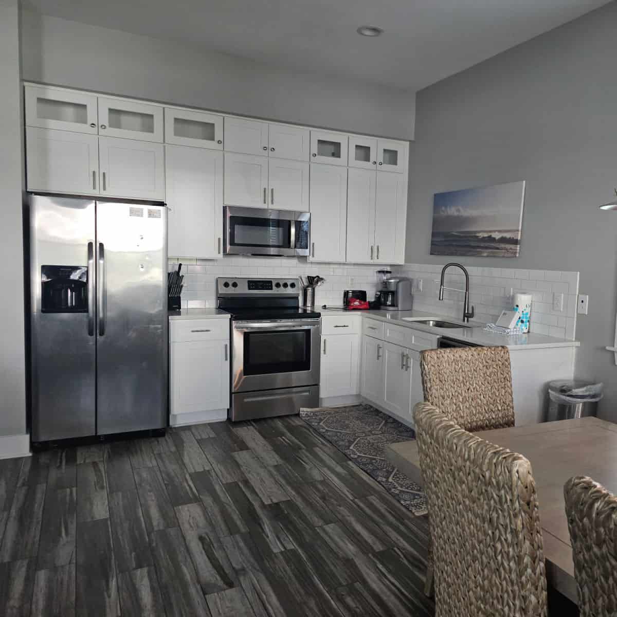 white kitchen cabinets with stainless steel appliances on two walls, dining room table with rattan chairs near the wall