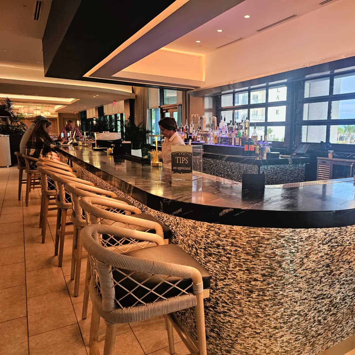 Indoor bar with a female bartender and tall chairs pulled up to the bar