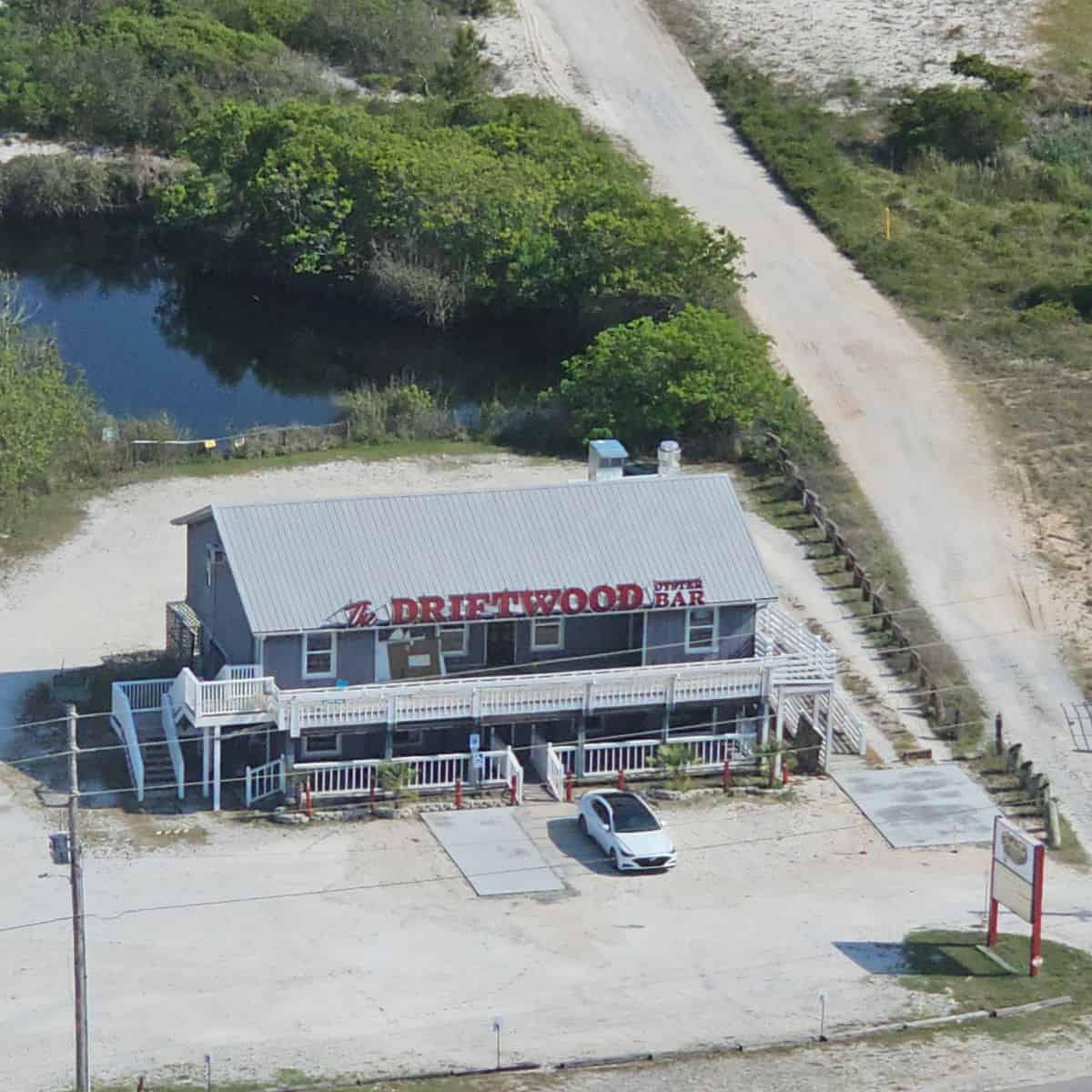 Looking down over the Driftwood oyster bar building, pond in the background with dirt road along the side