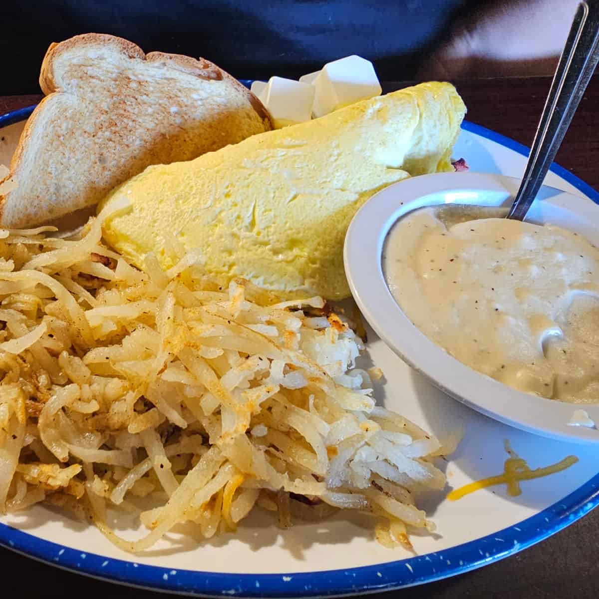 omelet with bread, hashbrowns, and gravy on a white plate with blue rim