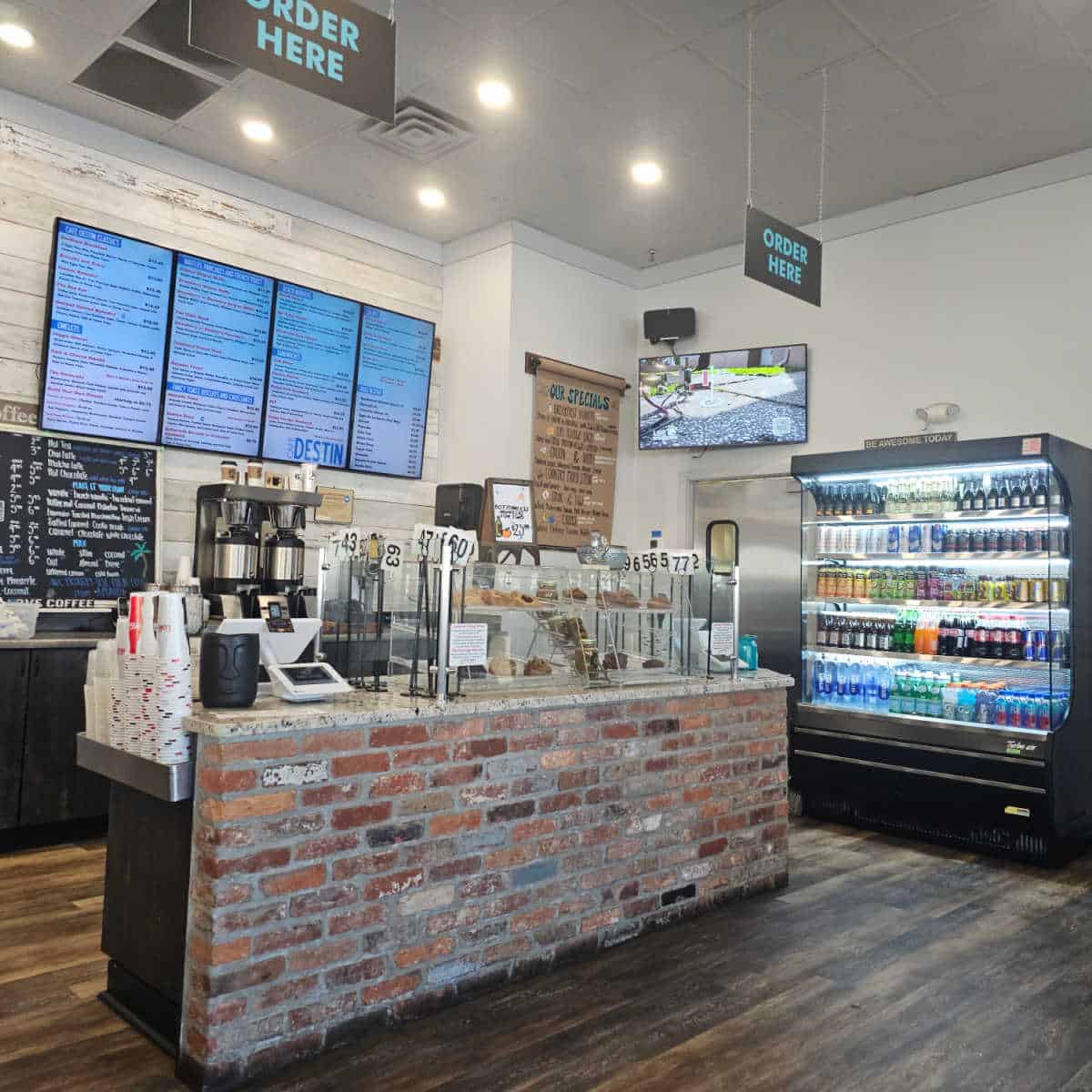 order counter with order here signs hanging over it, open cooler with drinks lined up, digital menu on the wall behind the counter