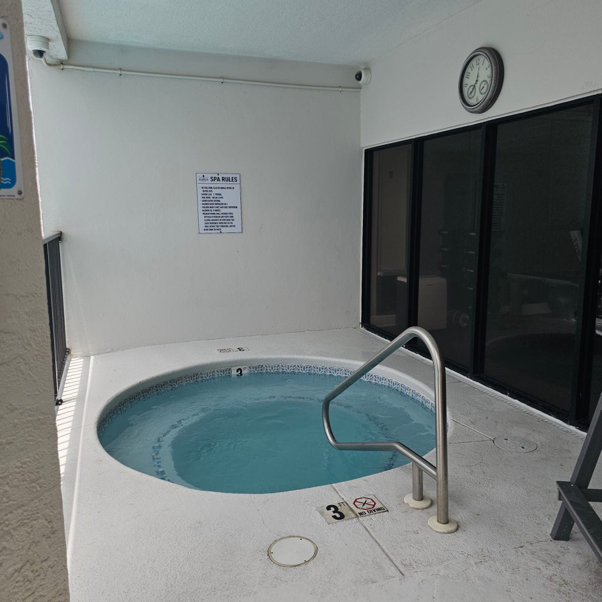 hot tub with spa rules sign above it under a cover with a clock on the wall
