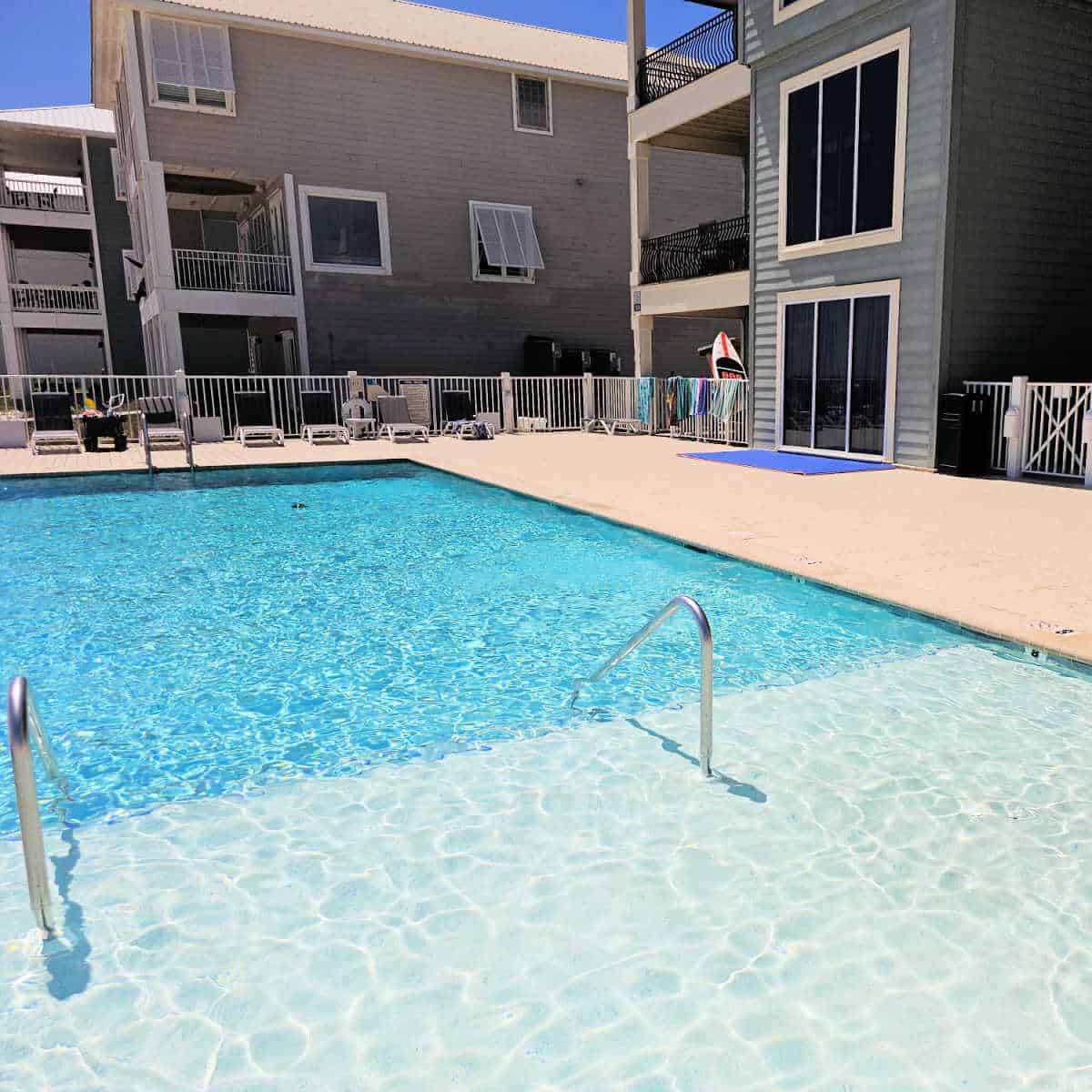 Outdoor pool with lounge chairs around the pool deck, vacation rental house next to the pool