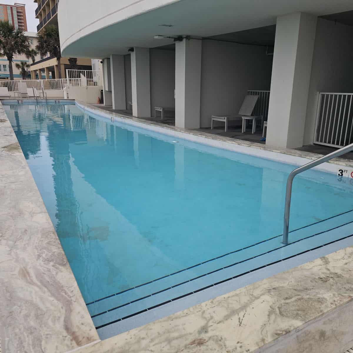 Outdoor pool with a couple of steps down into it. Chairs and tables along the edge of the pool