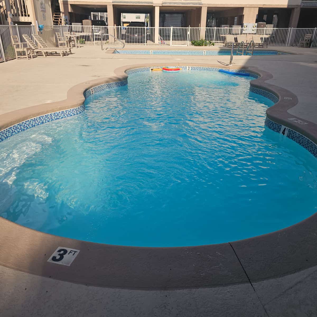 curvy outdoor pool with another pool in the background and lounge chairs