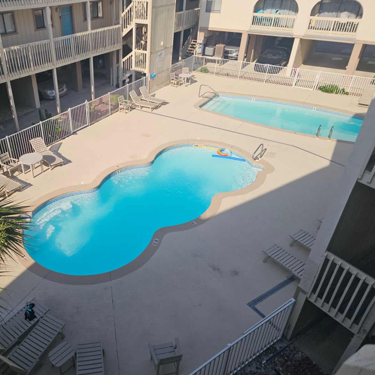 looking down on two outdoor pools and pool deck in between buildings