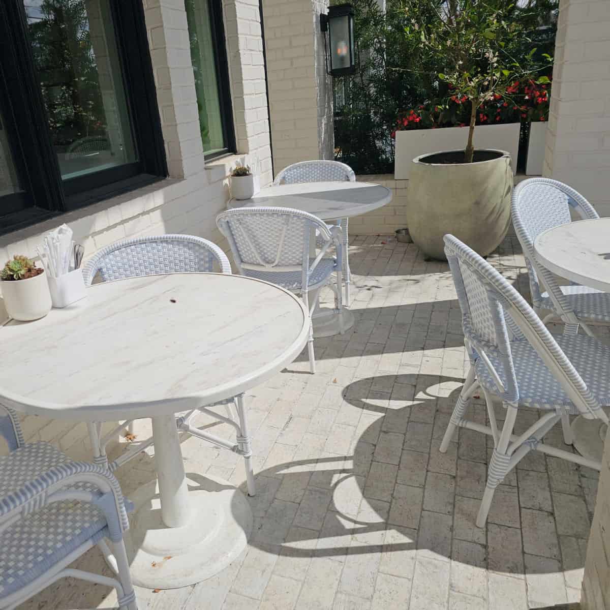 white tables and chairs outdoors on a brick patio with a plant in the background