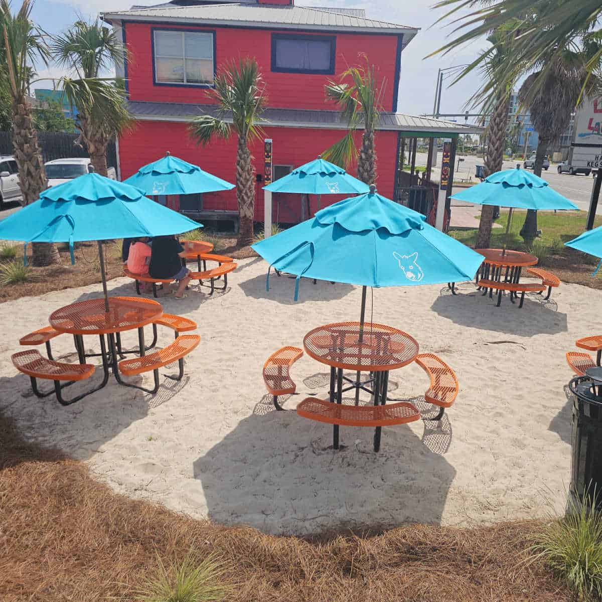 sandy outdoor seating area with orange circle tables and turquoise umbrellas with a donkey on them