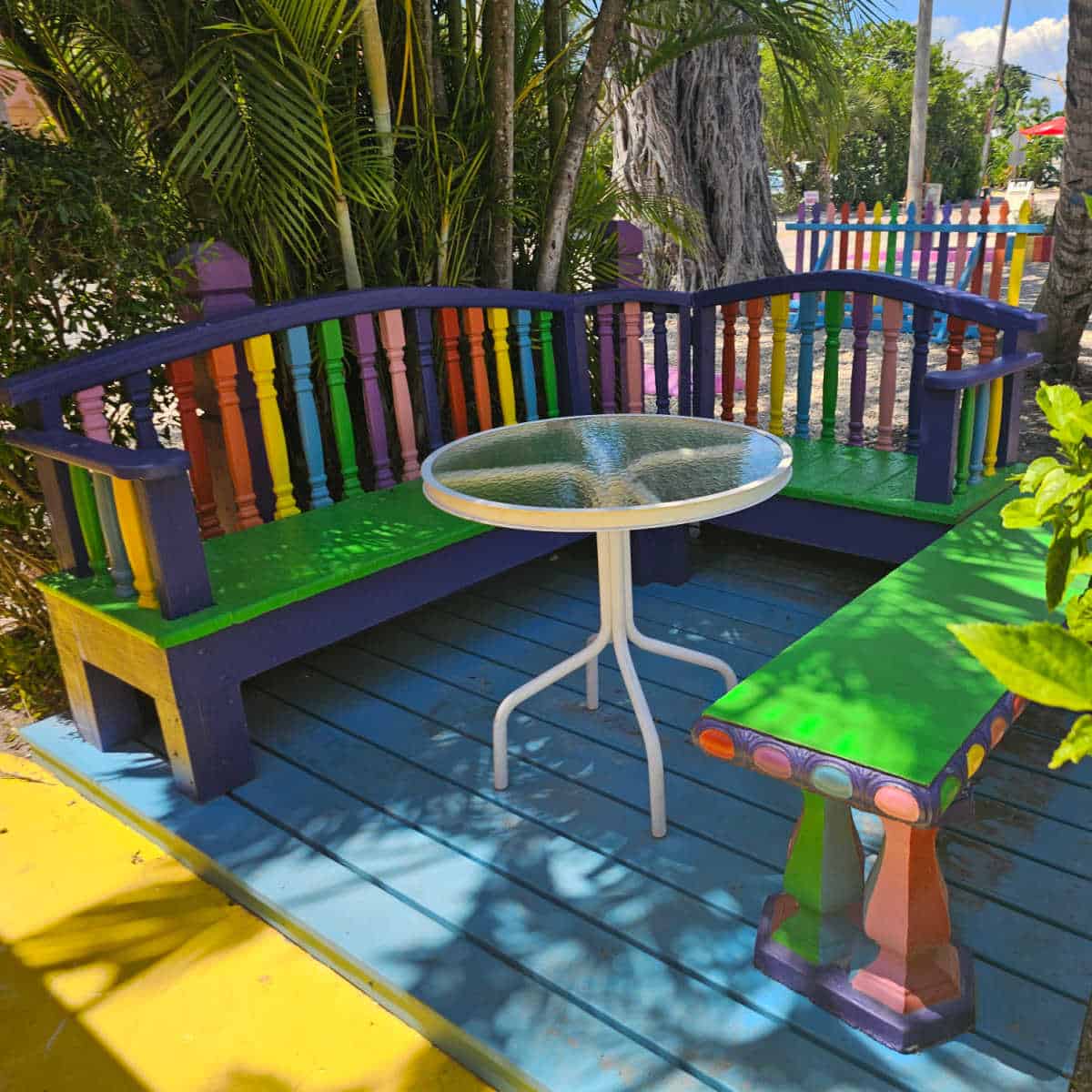 outdoor seating in the shade with rainbow painted back of the bench, a circle table, and bench