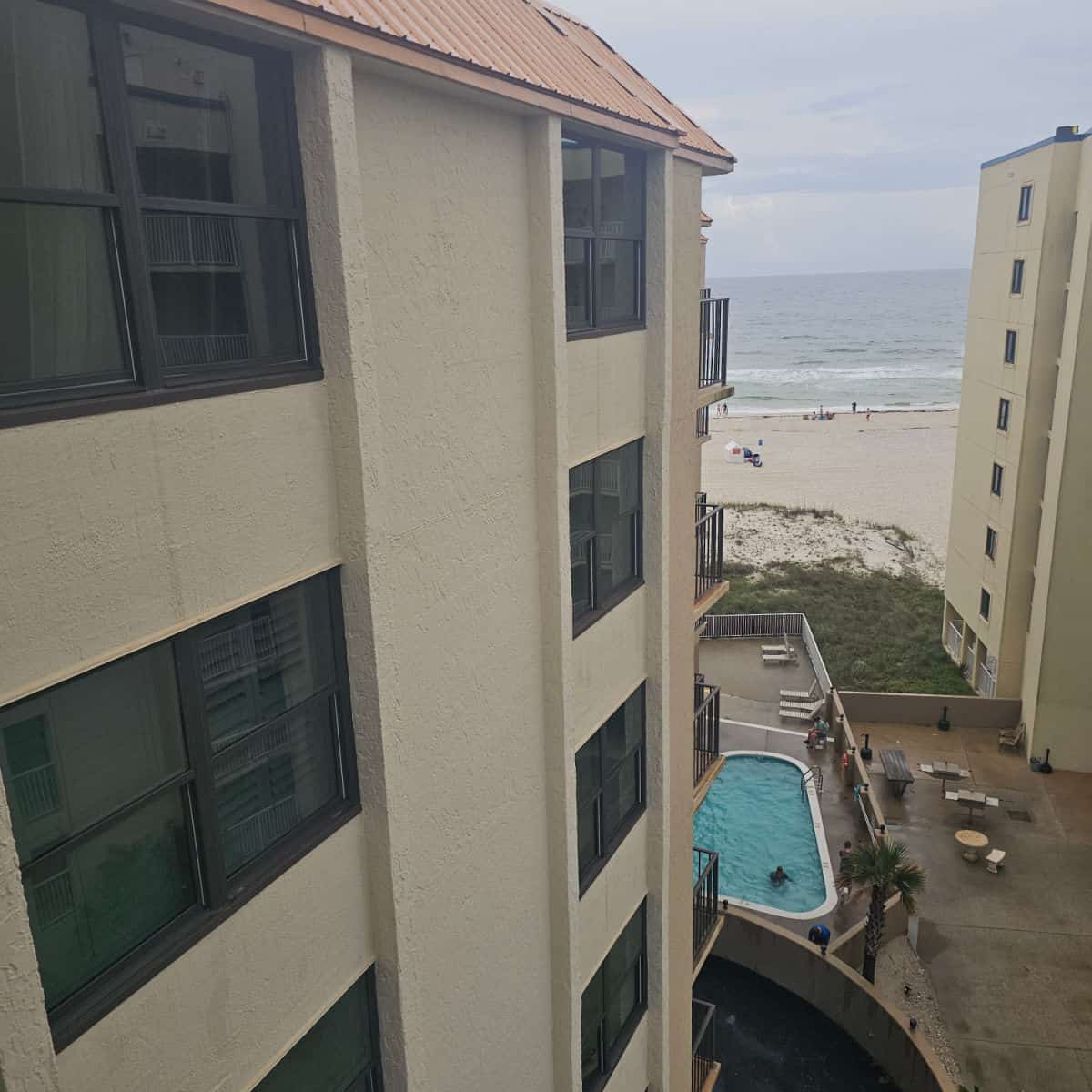 Looking down the side of a tan building with a pool on the side and the Gulf Shores beach and Gulf waters