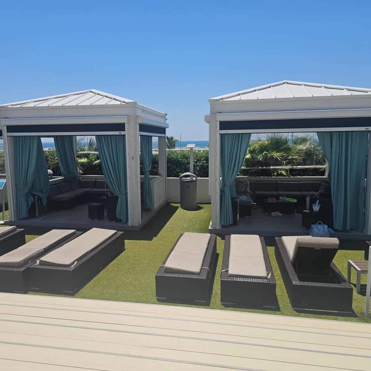 two cabanas with lounge chairs outside of them on fake green grass