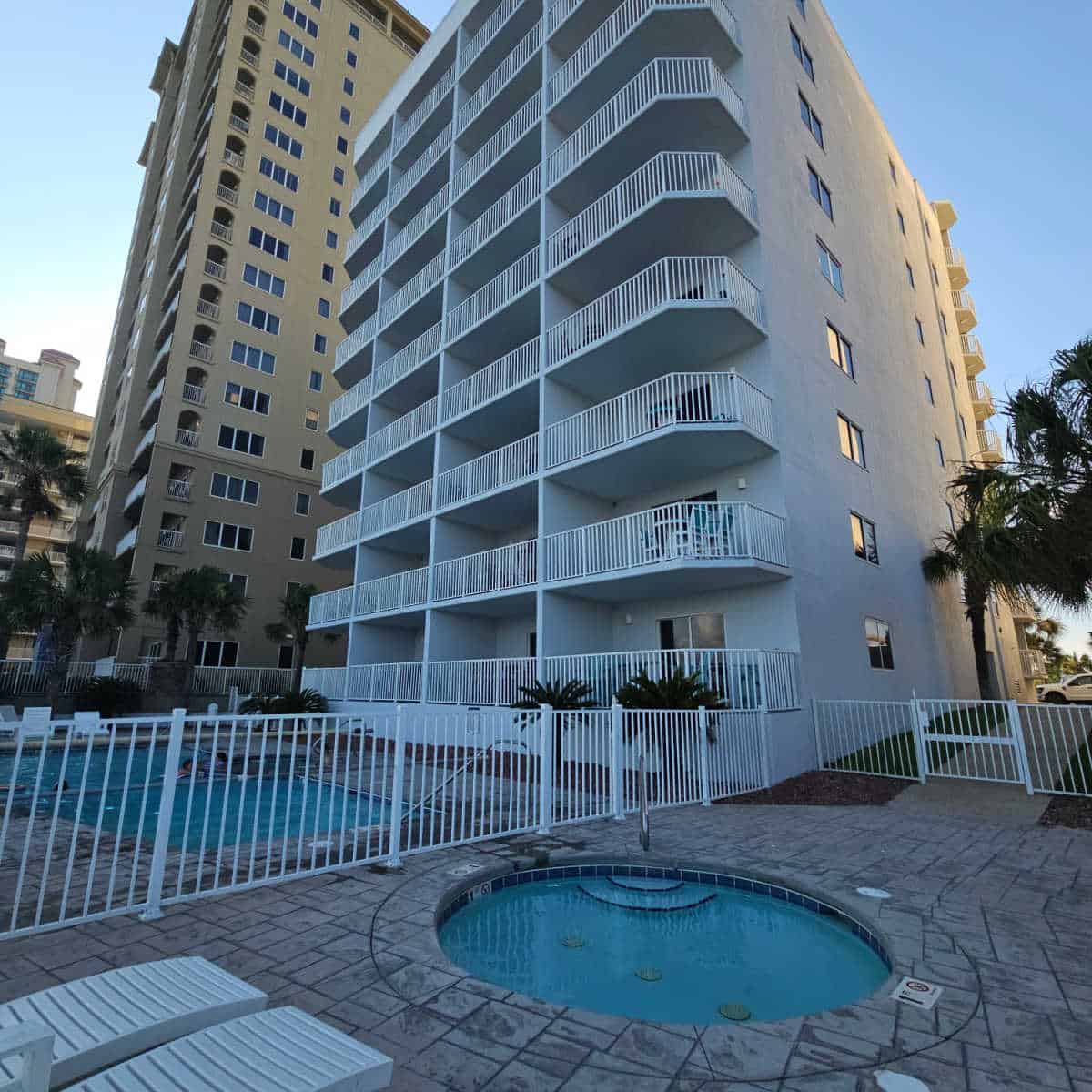 small circle kids pool behind a fence with a larger fence to the left, Four Winds condo building behind the pool
