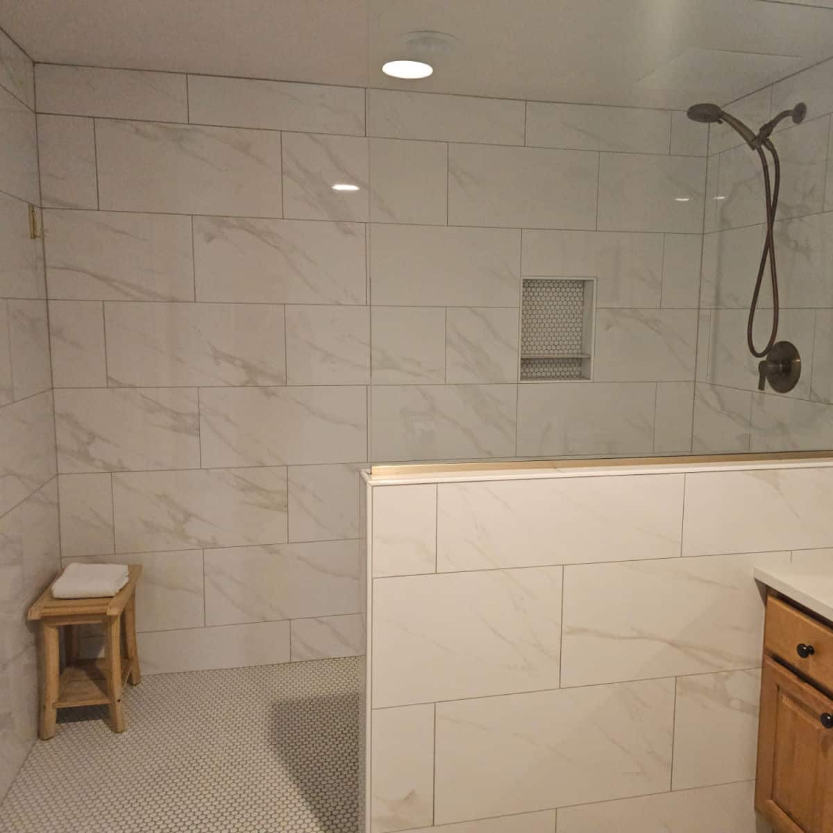 large walk in shower with a bench in the corner, towel on top of the bench