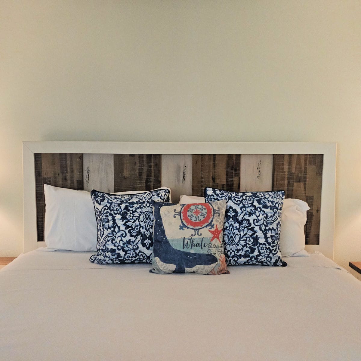 bed with white linens, pillows stacked in front, and a wooden headboard