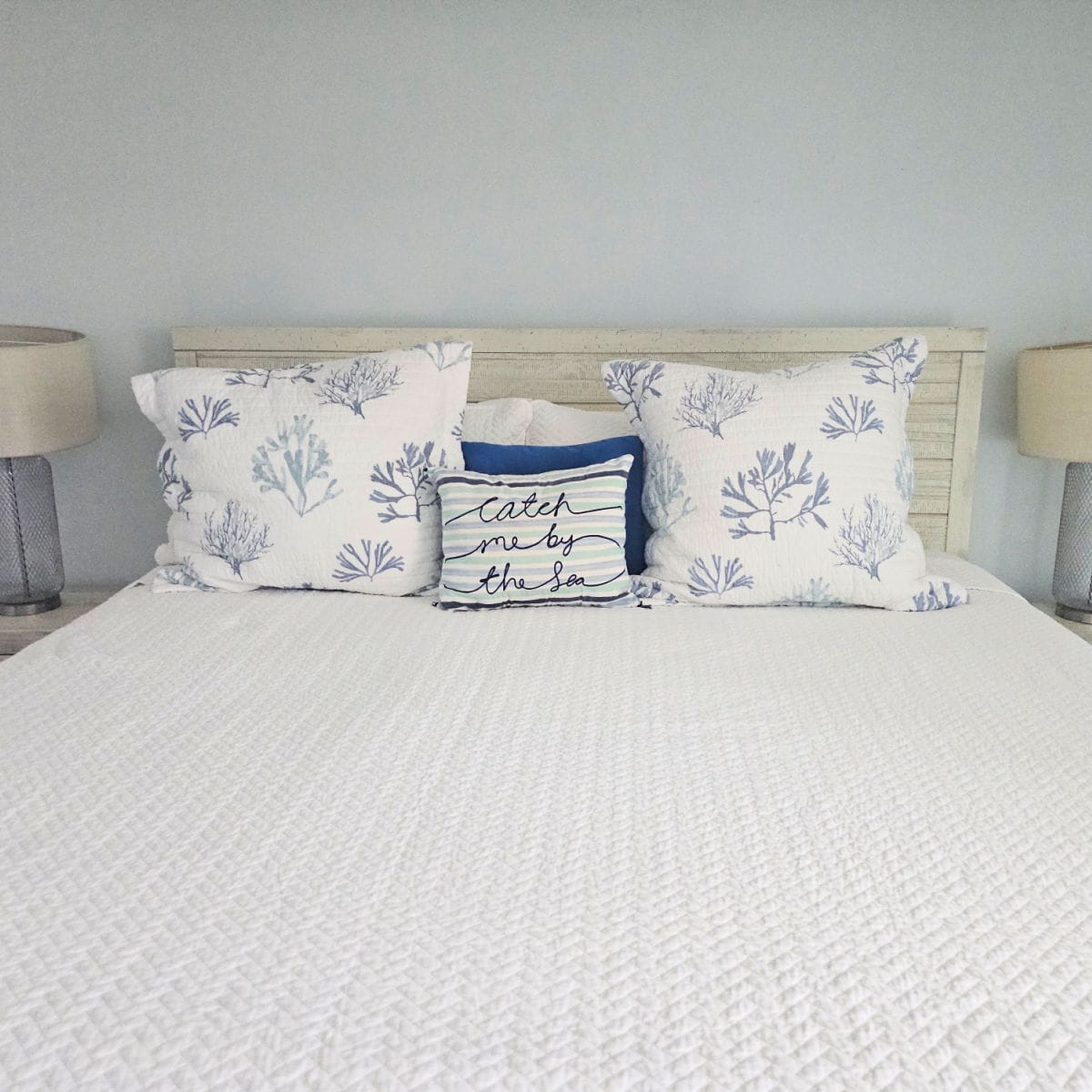 bed with catch me by the sea pillow and sea fan pillows, lamps on either side of the bed