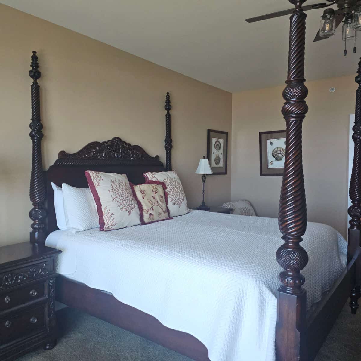 big wooden bed with white linens, red and white pillows, nightstand next to the bed,