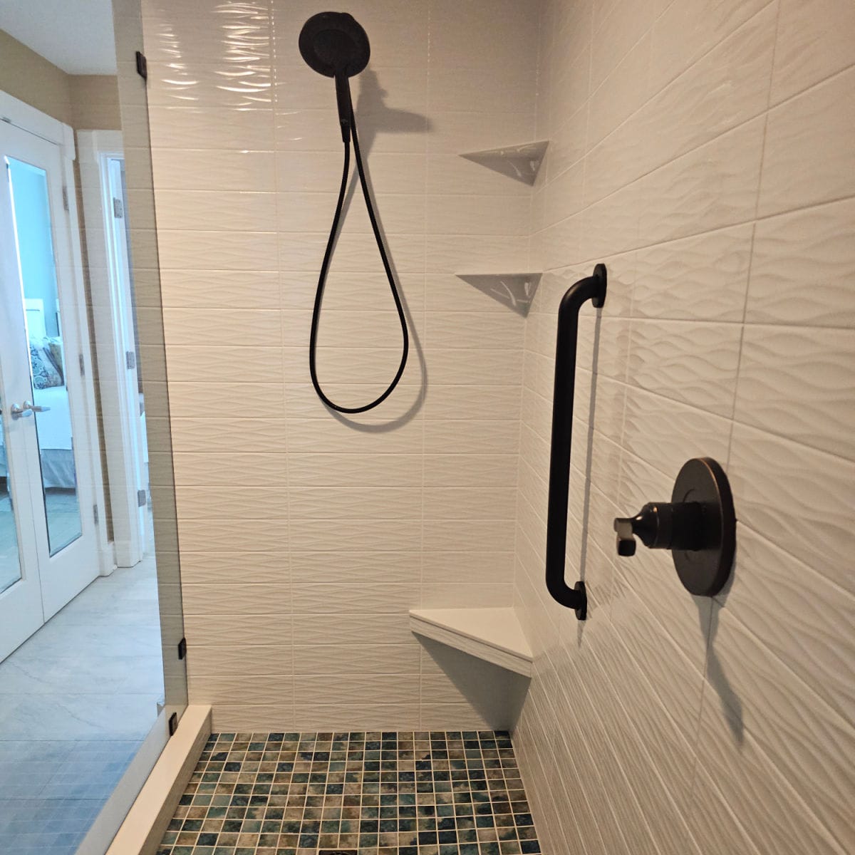 Shower with white tiles, colorful floor tiles and a low entry step, mirrored closet on the other side of the bathroom