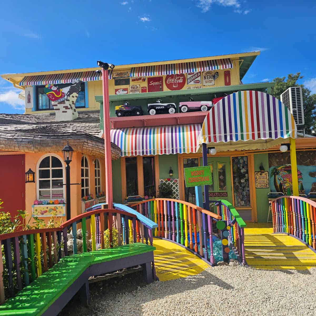 Rainbow paint on the walkway, awnings leading to the Bubble room restaurant, toy cars, and Coke signs on the building along with Santa on a sleigh art