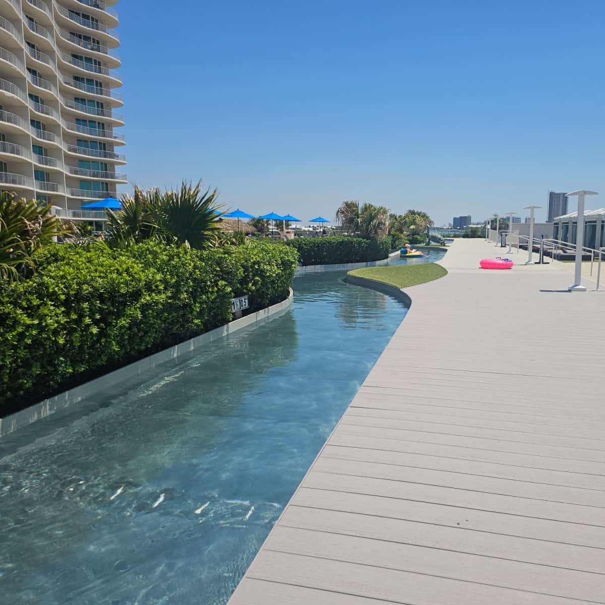 lazy river running along a pool deck with plants in the middle, building on the left side