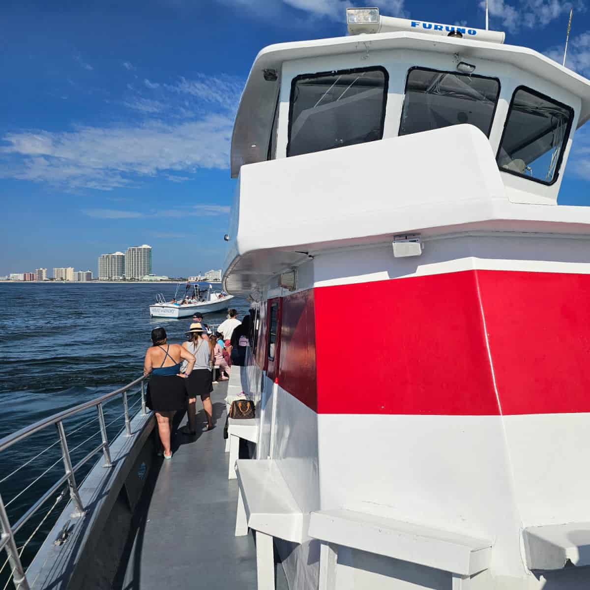 looking down the side of a white boat with a red stripe, people at the end of the boat