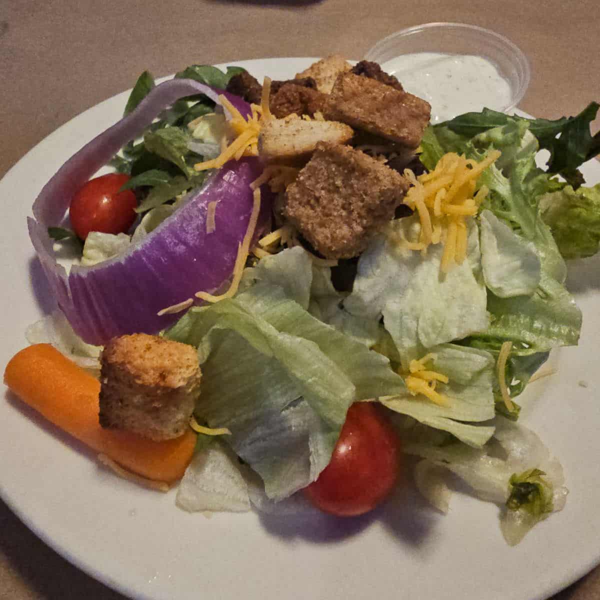basic salad with croutons on a white plate with a container of ranch