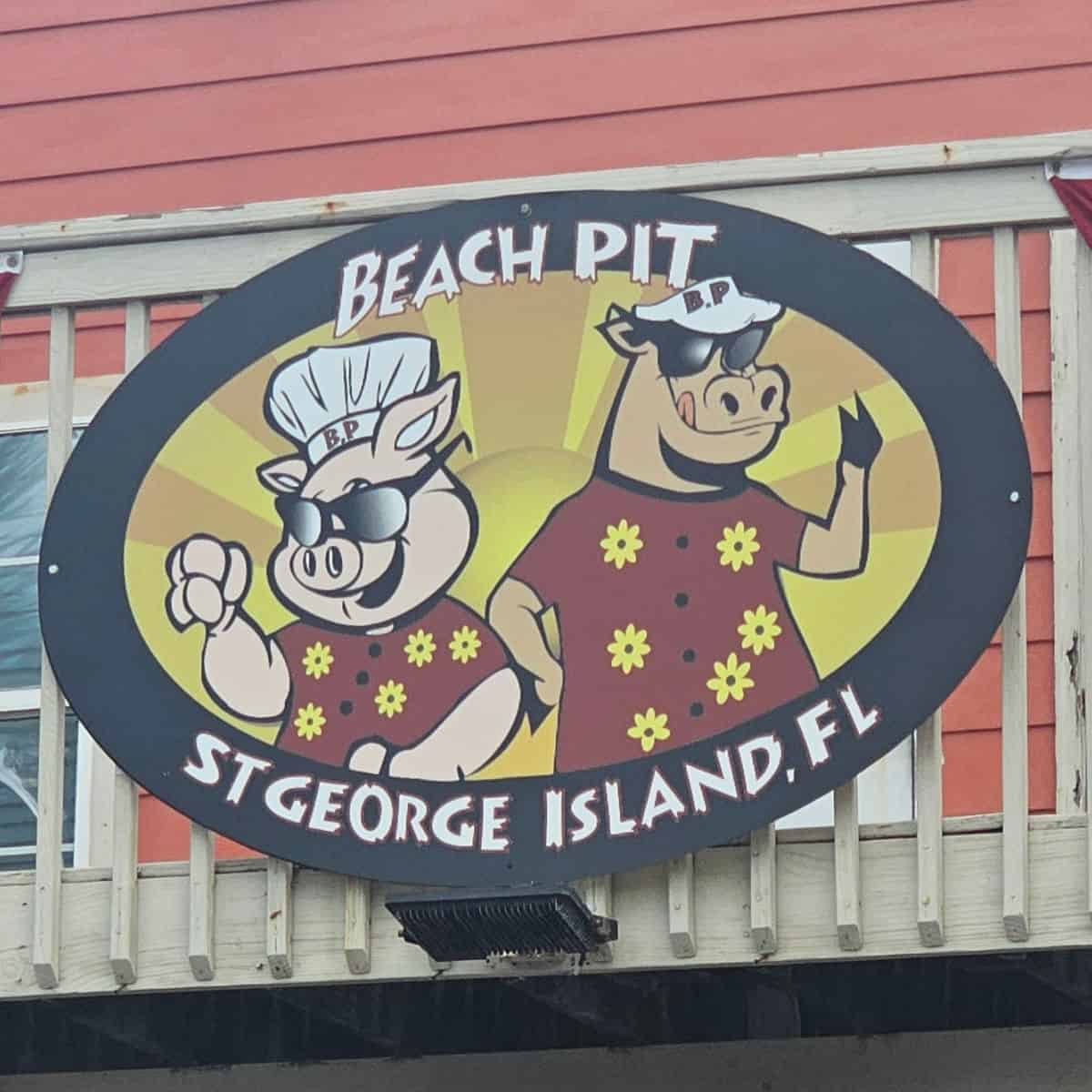 Beach Pit St George Island sign with a pig and a cow wearing sunglasses and red shirts with yellow flowers on them