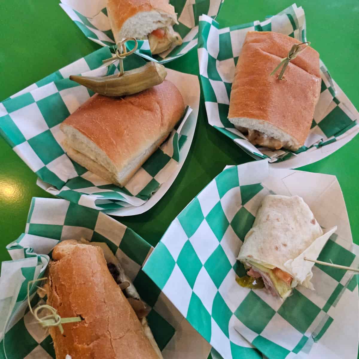 green table with green and white checkered paper baskets filled with subs and wraps