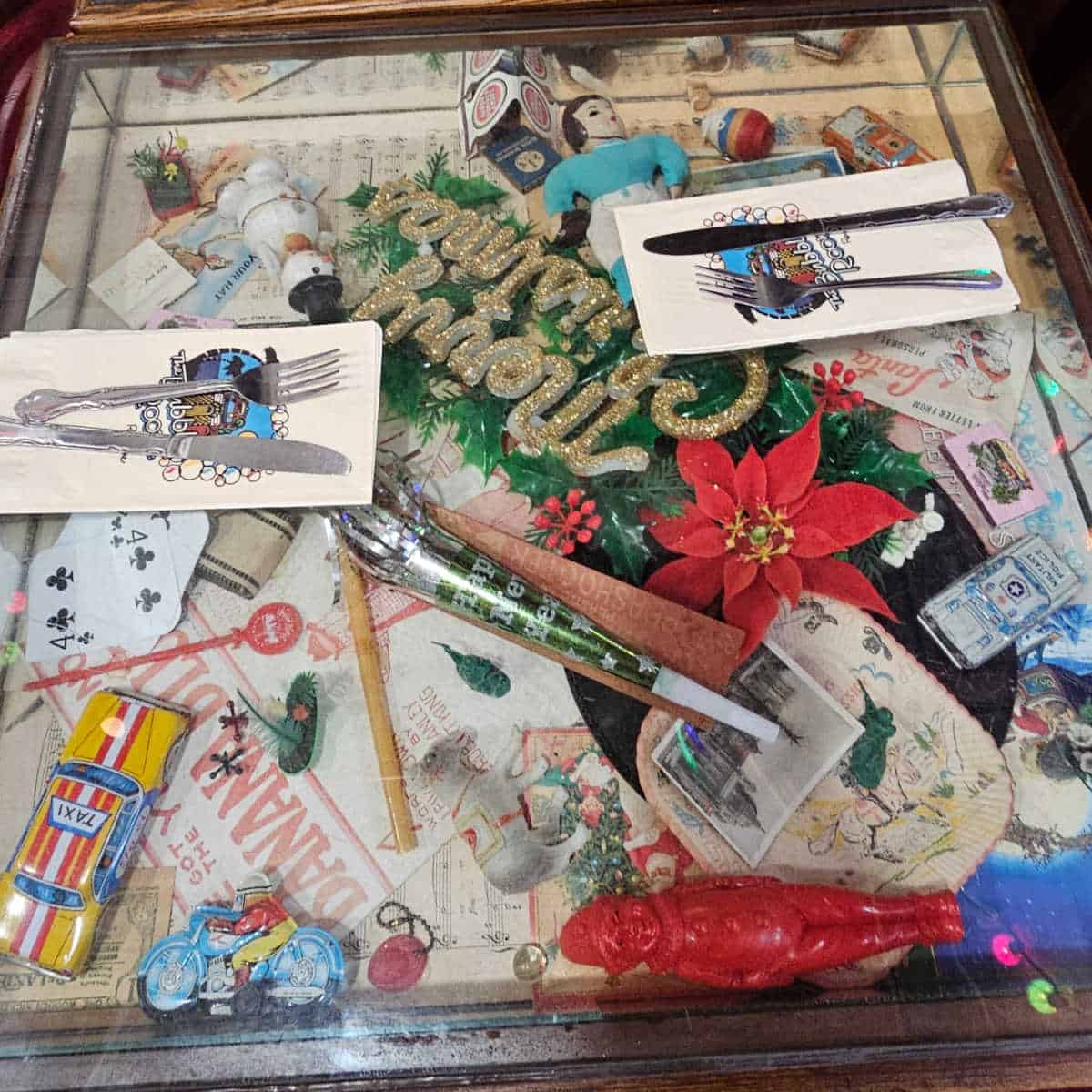 table with christmas decorations, toys, match books and other souvenirs under the glass, bubble room napkins with fork and knife on top