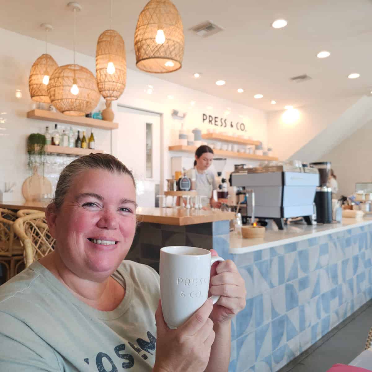 Tammilee holding a Press & Co mug with the order counter behind her