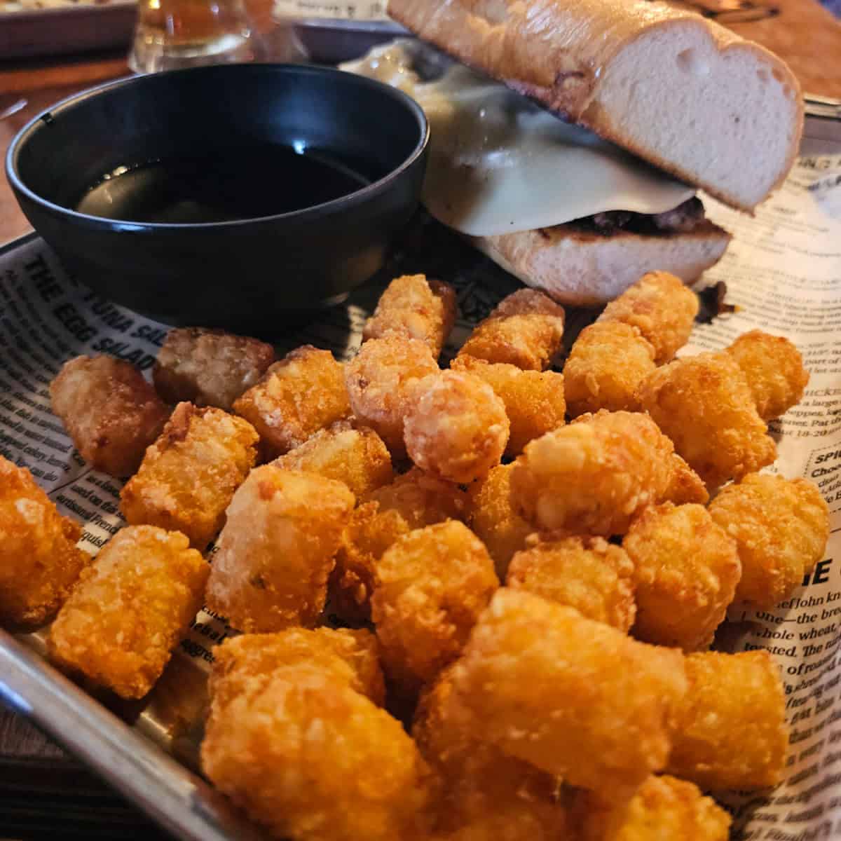 platter with a tater tot, bowl of sauce, and cheesesteak