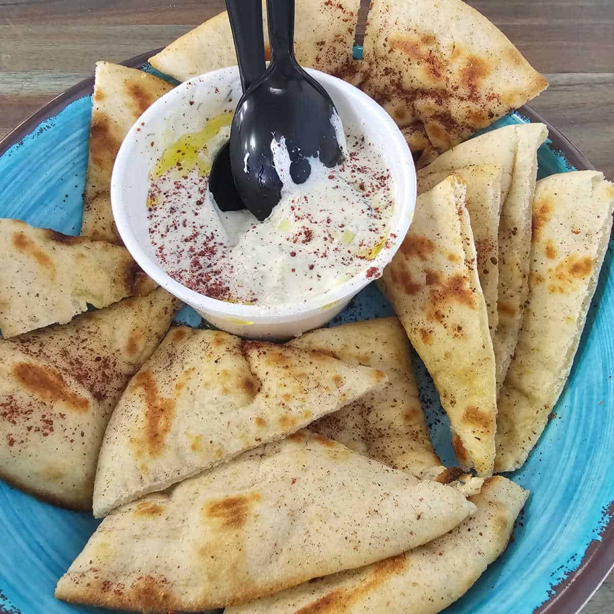 Tzatziki in a white bowl with triangles of pita around the bowl on a turquoise plate