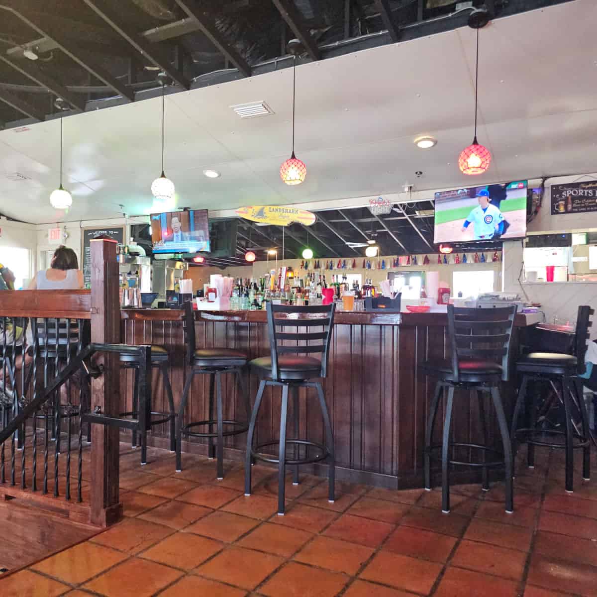 tall bar stools next to a bar with tvs in the background
