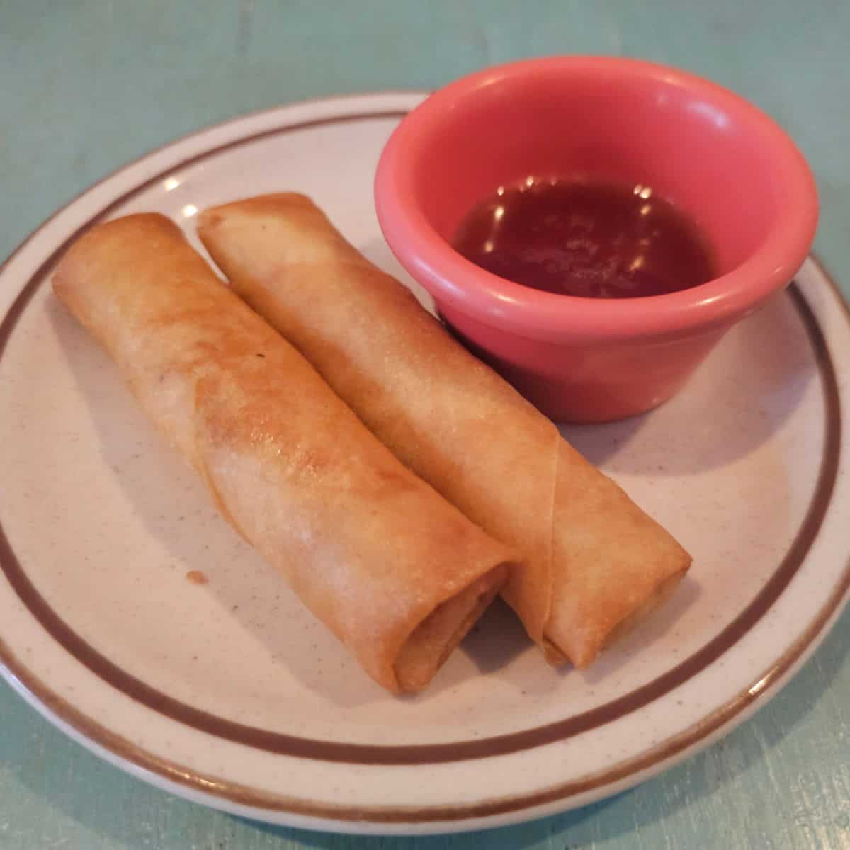two egg rolls next to a bowl of sauce on a white plate