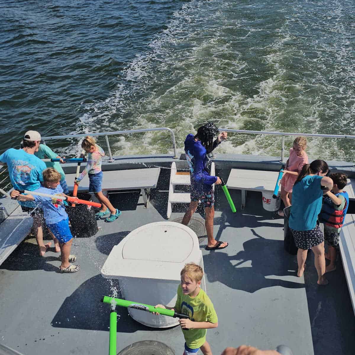 back of a boat with adults and kids holding water guns, water in the background