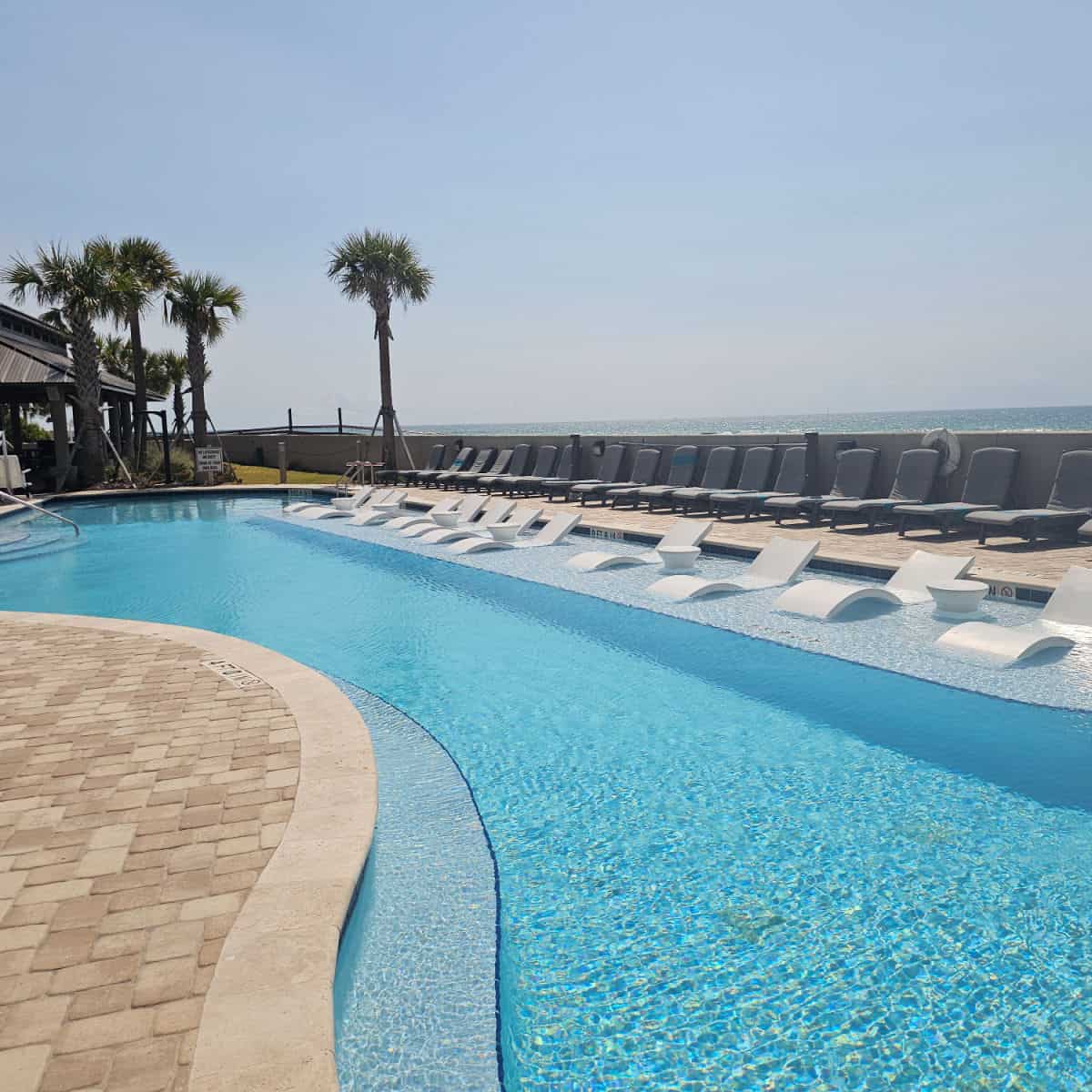 adults only pool with white chairs and tables along a ledge in the pool, looking out towards the Gulf water