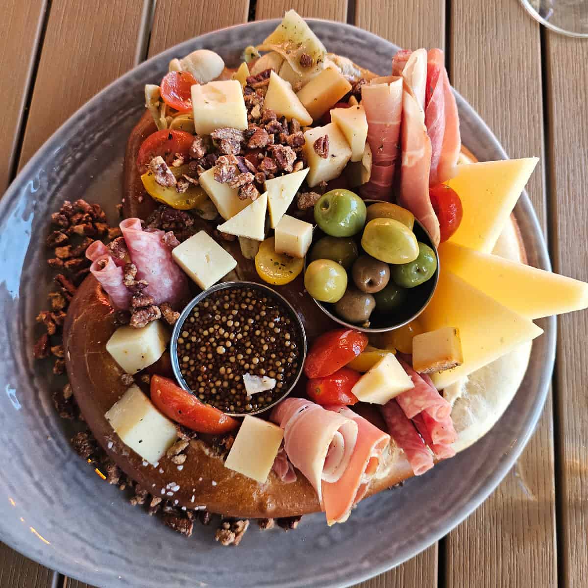 Pretzel charcuterie board with meats, cheese, olives, and nuts on a blue plate