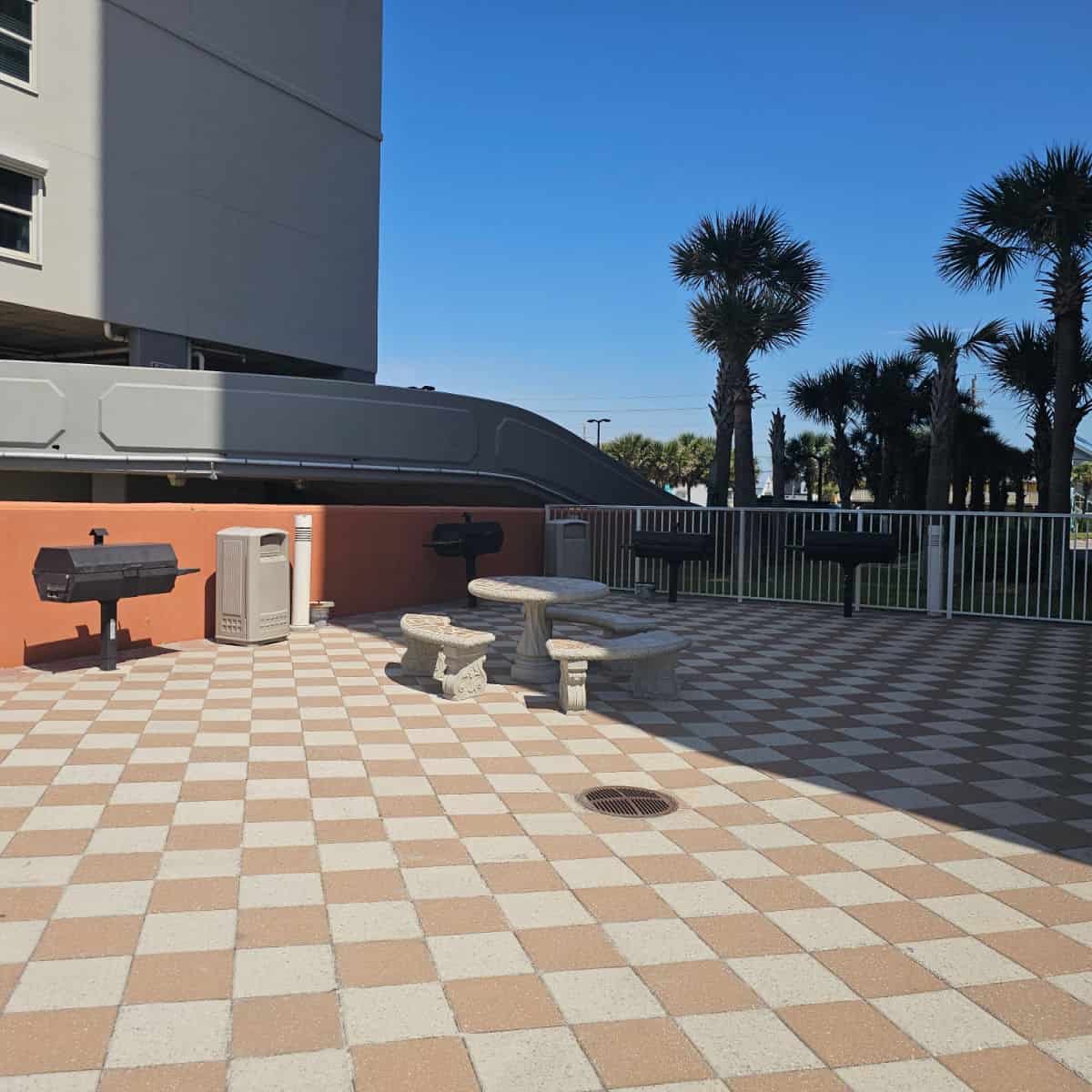 checkered outdoor tile patio, four large barbecues on the patio with a concrete table and benches