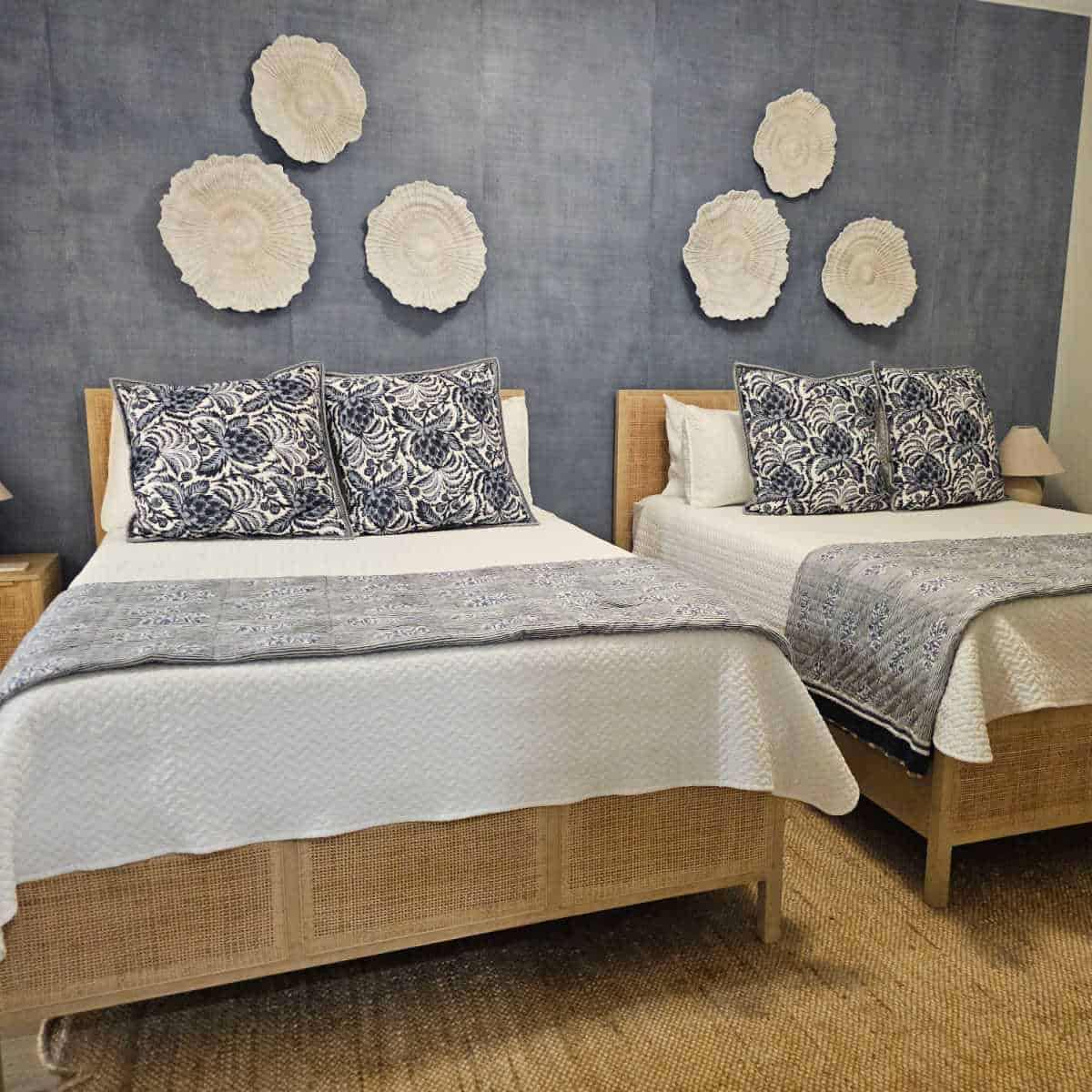 Bedroom with a blue wall with white flower art attached, two beds with white linens and blue and white pillows