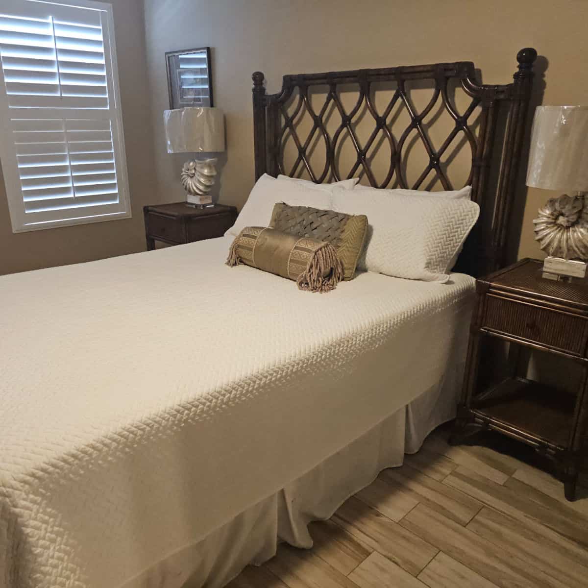 bedroom with tan walls, bed with wooden bedframe, two nightstands with shell base lamps and decorative pillows on the bed
